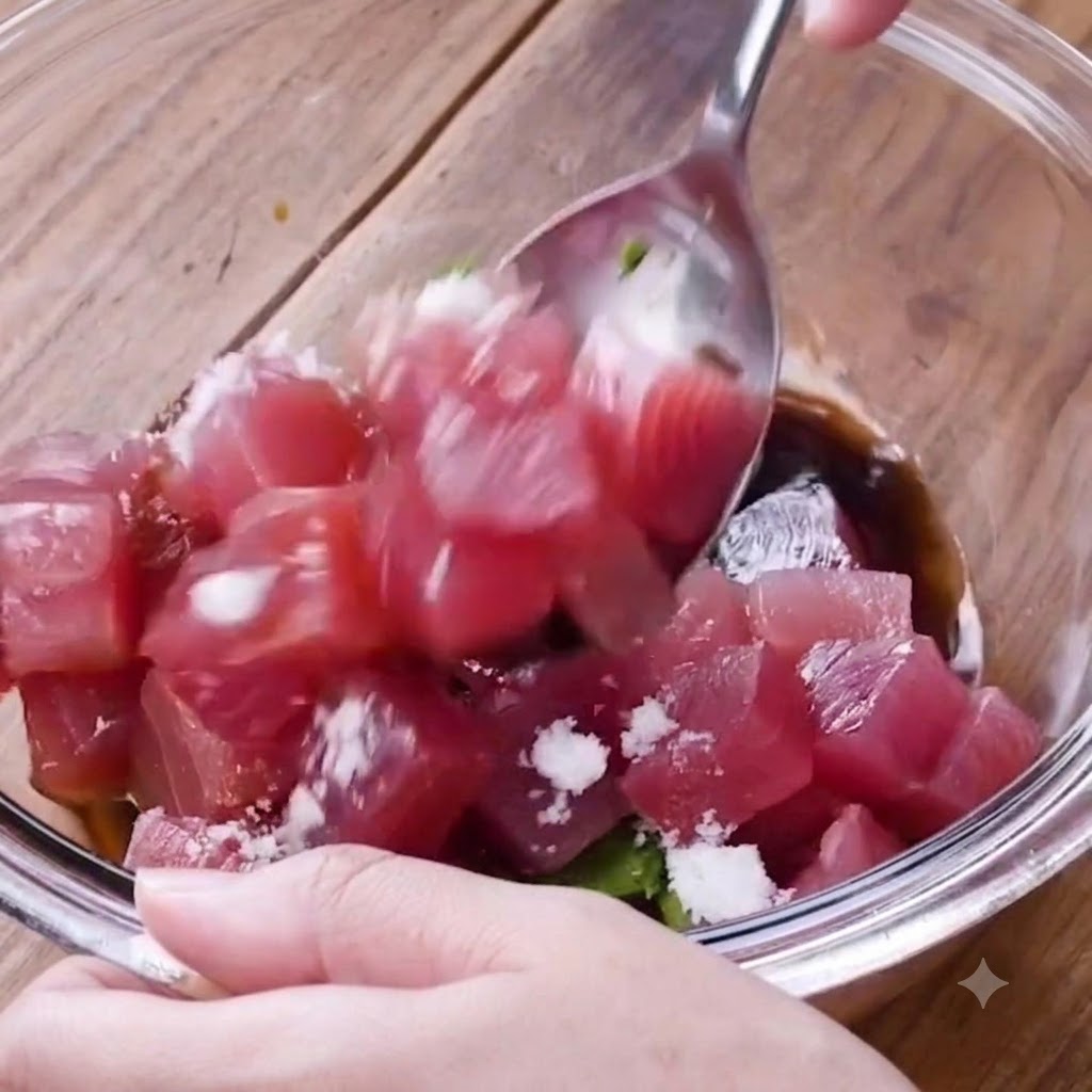 A spoon mixing cubed tuna and avocado with seasonings in a glass bowl.