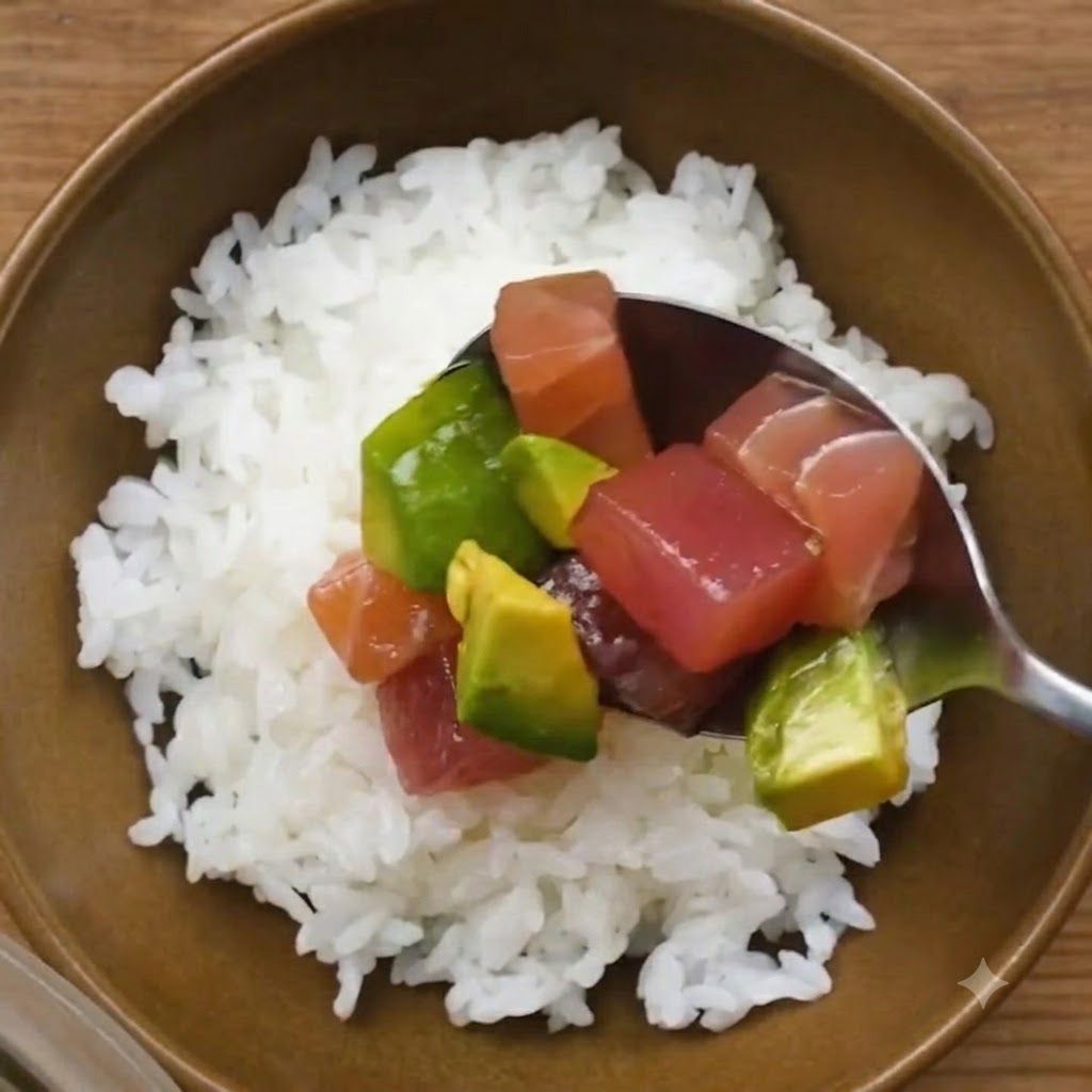 A spoonful of marinated tuna and avocado being placed over a bowl of white sushi rice.