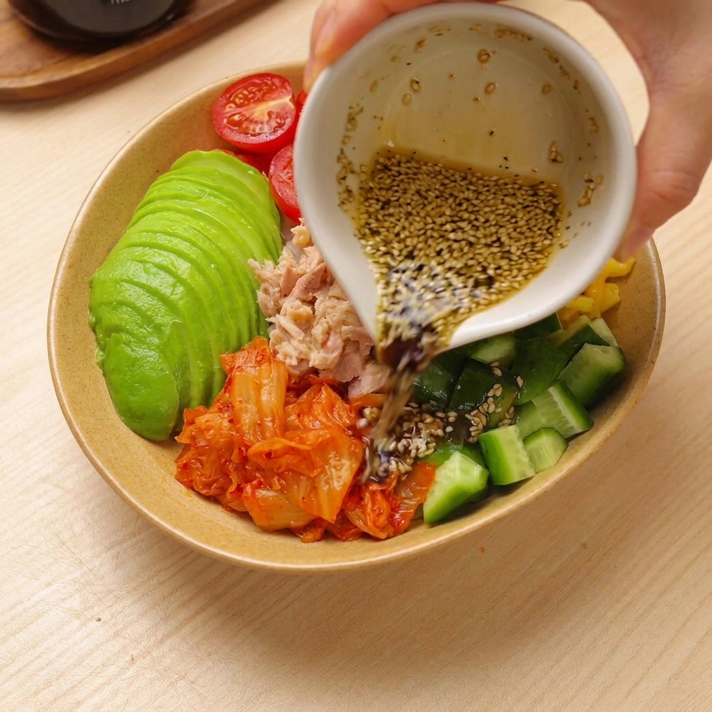 Dressing being poured over a colorful assembled tuna avocado rice bowl.