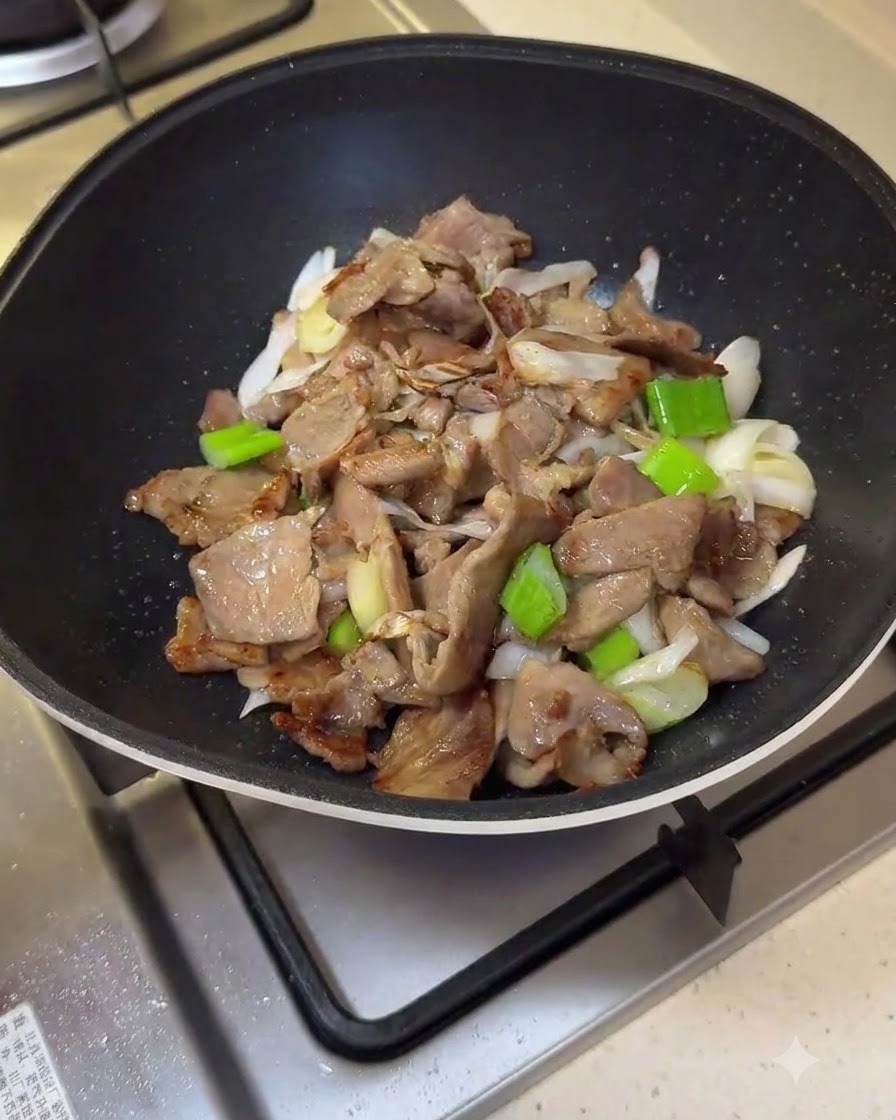 Red sauce mixture being poured into the frying pan over pork and scallions.