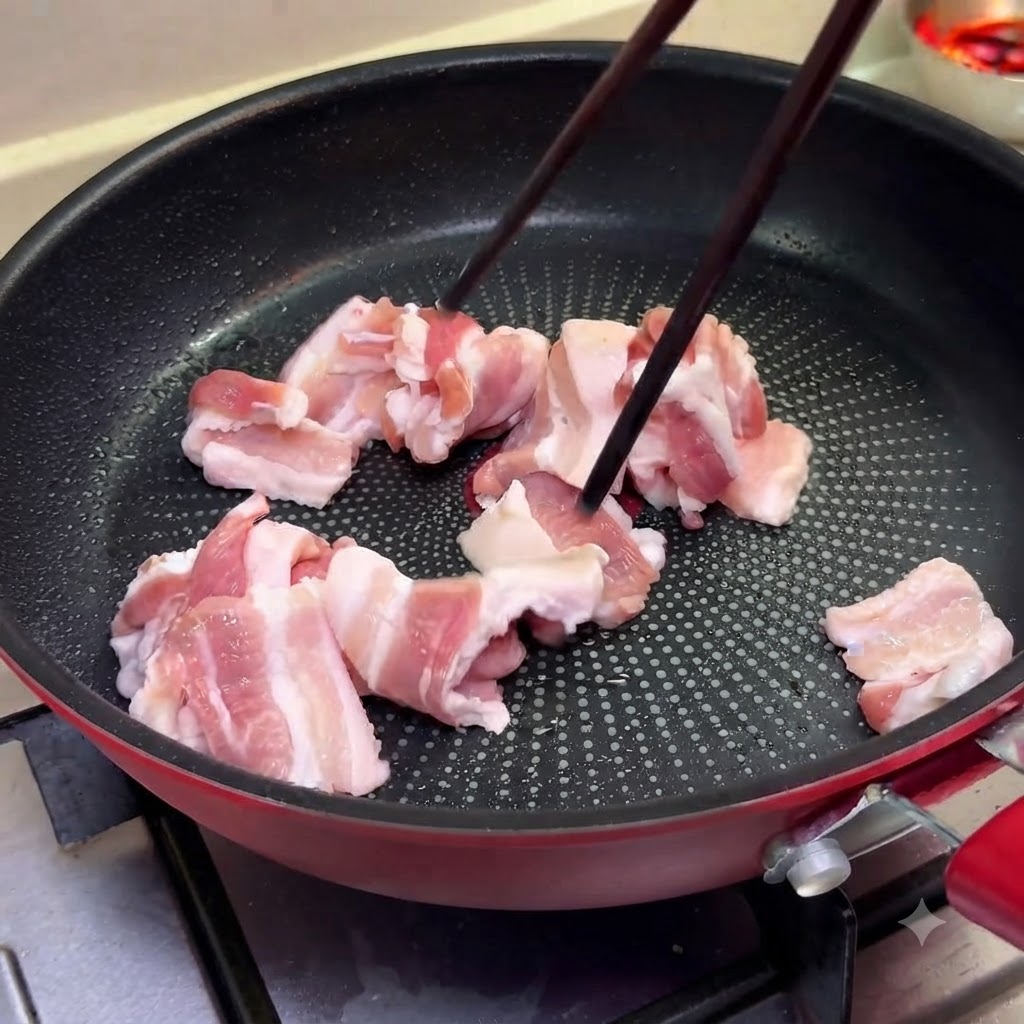 Thin slices of pork belly cooking in a pan over medium heat using chopsticks.