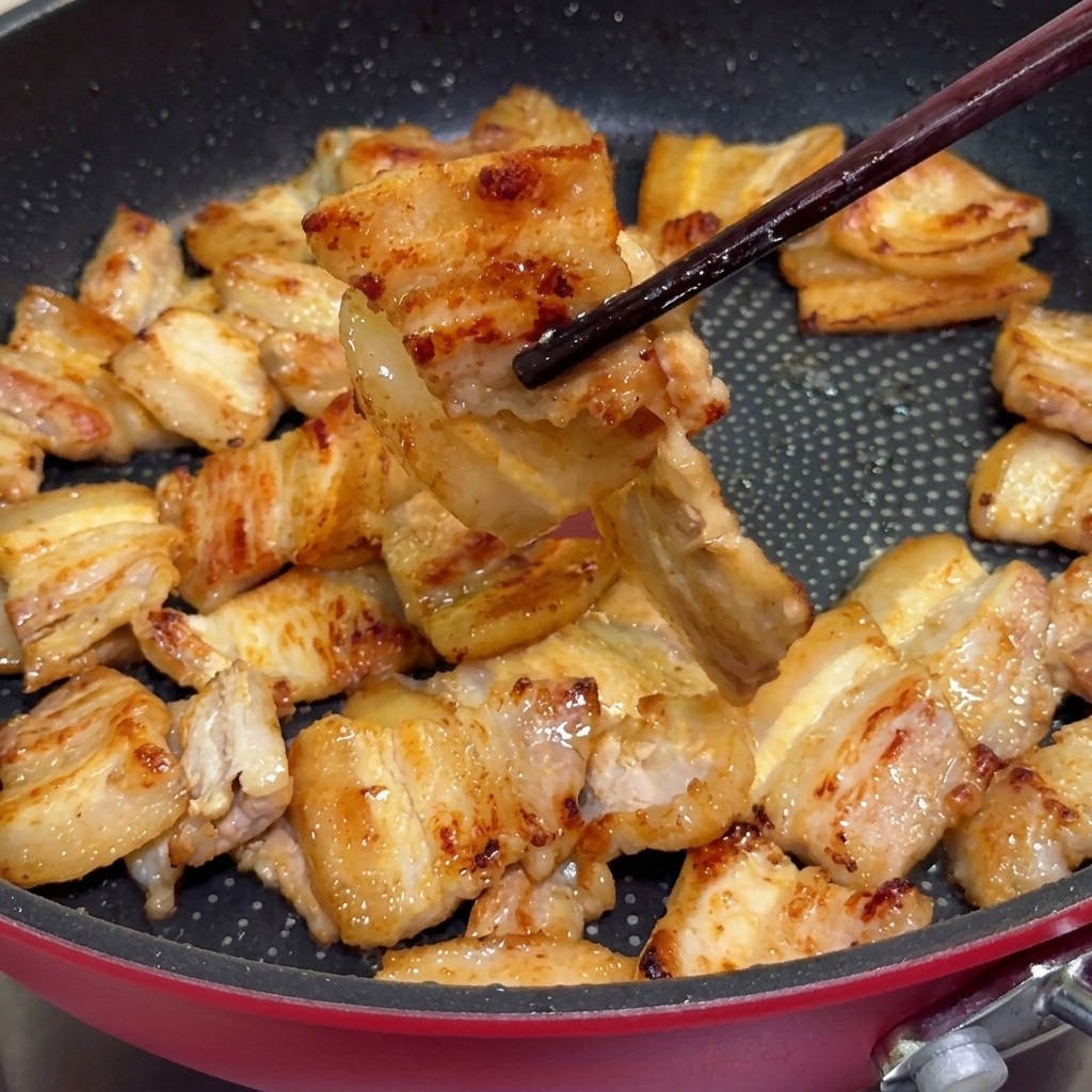 Sliced onions being stir-fried in the pan using chopsticks amidst rendered pork fat.