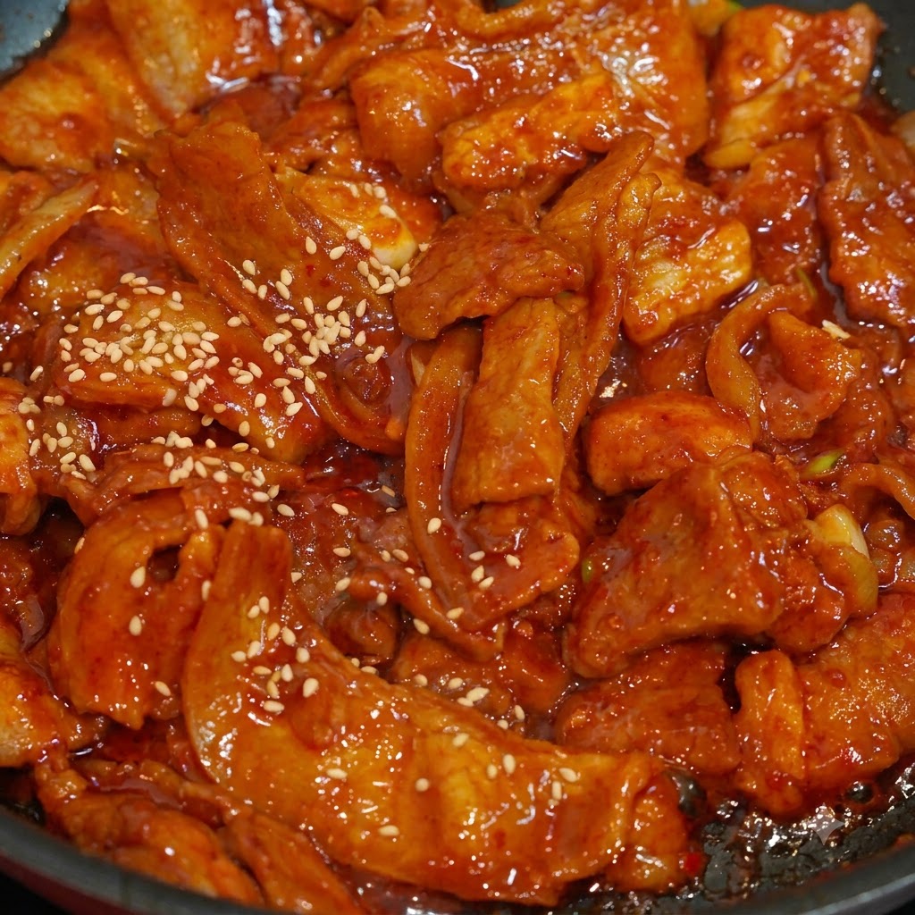 A close-up shot of white sesame seeds being sprinkled over vibrant red, saucy spicy pork slices in a frying pan.