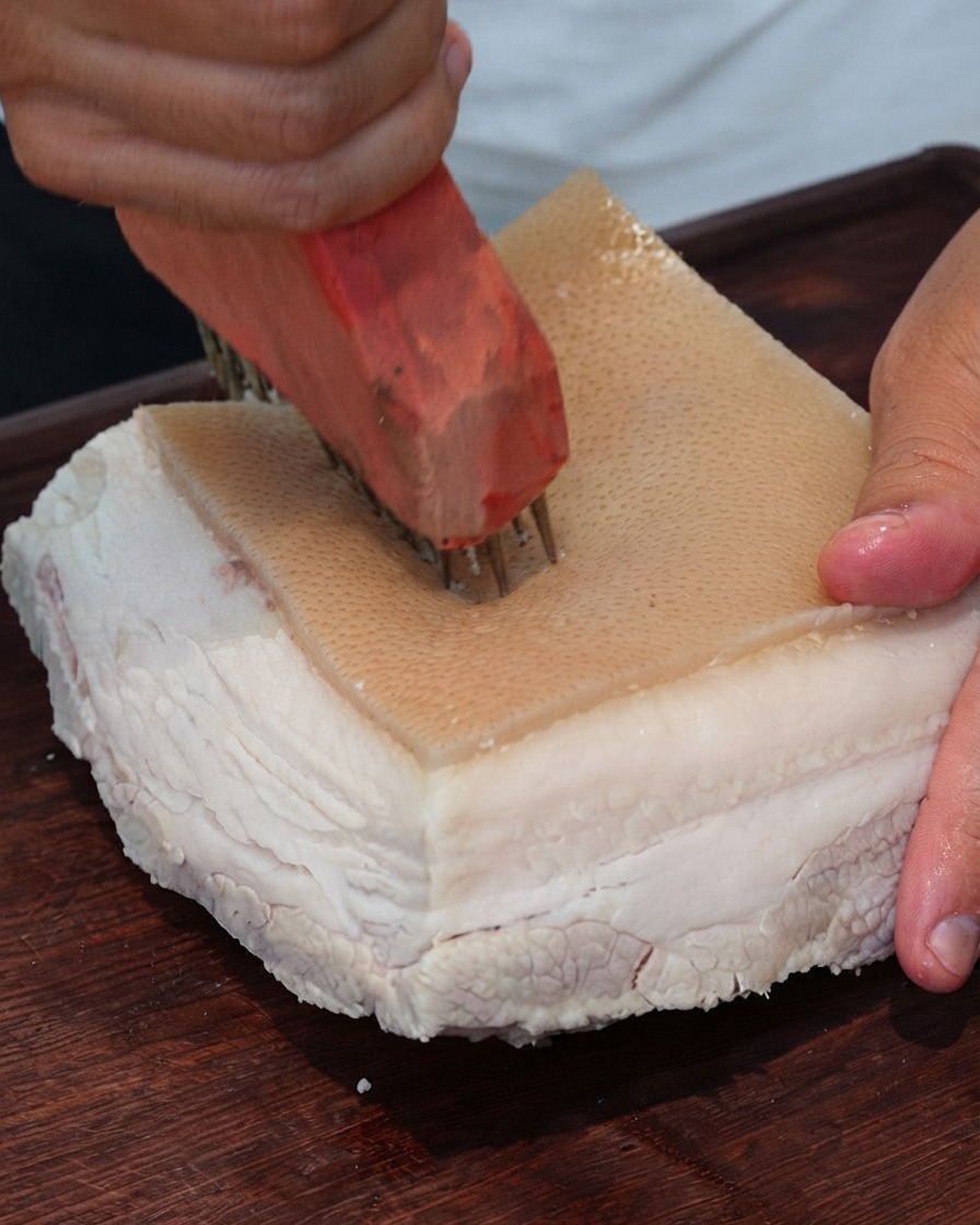 Close-up of a meat pricking tool repeatedly punching holes into the surface of pork skin.