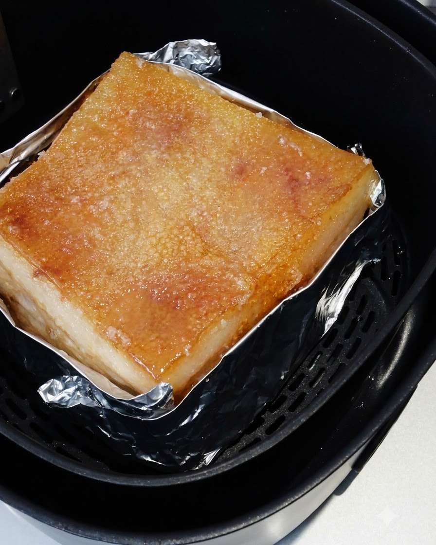 The roasted pork belly sitting inside the air fryer basket with its salted skin cooked to a golden hue.
