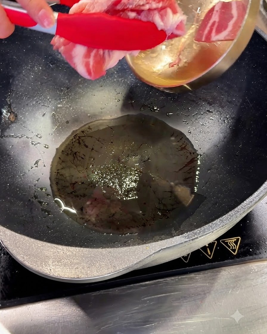Pork belly slices being added to hot oil in a wok using red tongs.