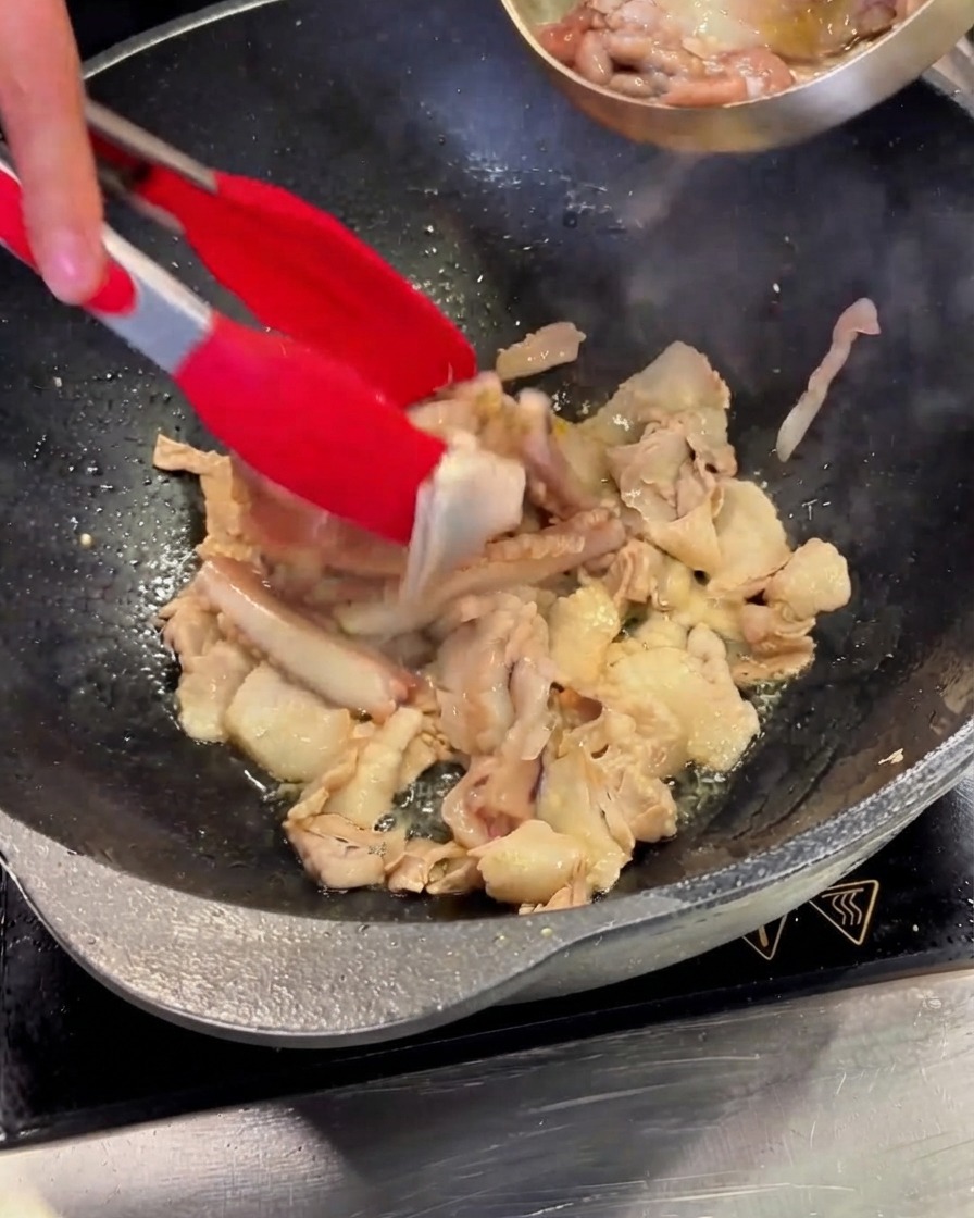 Cleaned squid pieces being poured from a steel bowl into the wok containing pork belly.