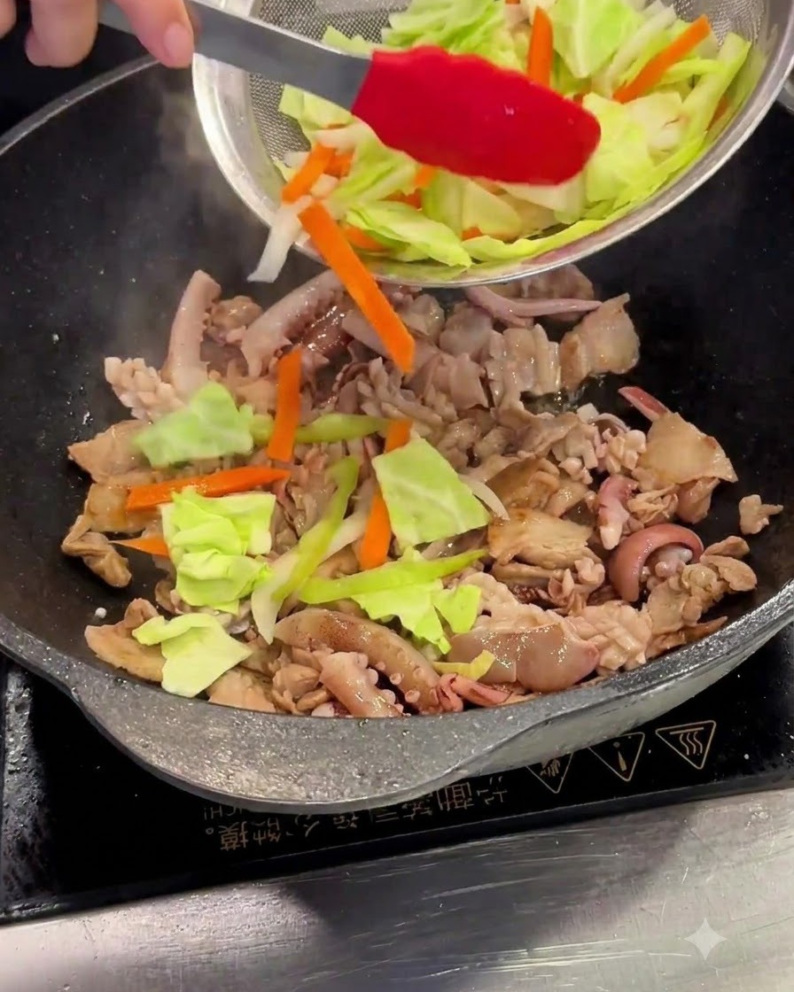 Sliced cabbage and carrots being added from a mesh strainer into the wok.