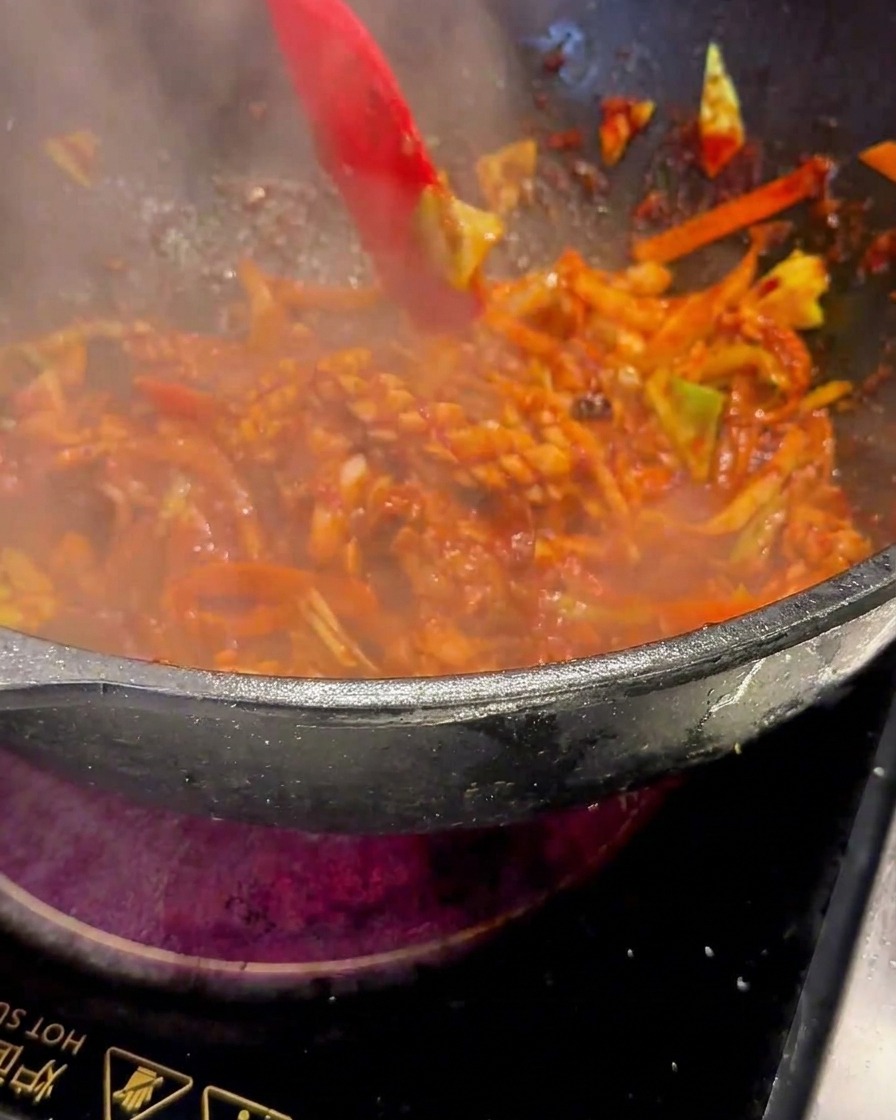 A red spatula stirring the sizzling mixture in the wok under hot heat.