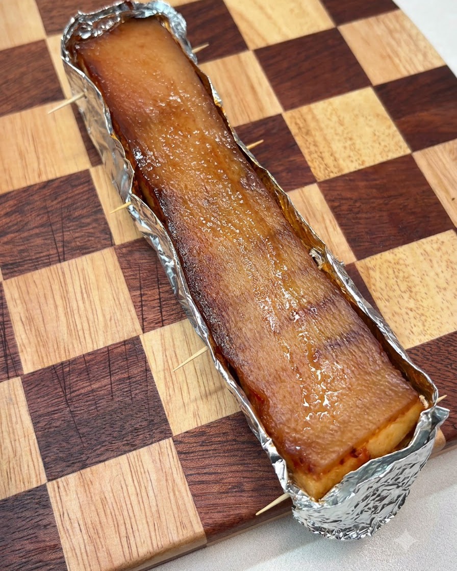 A thick layer of coarse salt evenly spread across the top surface of the pork skin wrapped in foil.