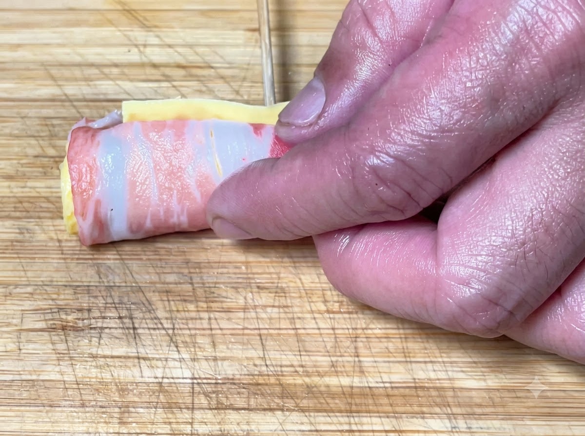 Hands rolling up the pork belly layers and securing the cylinder shape with bamboo skewers.