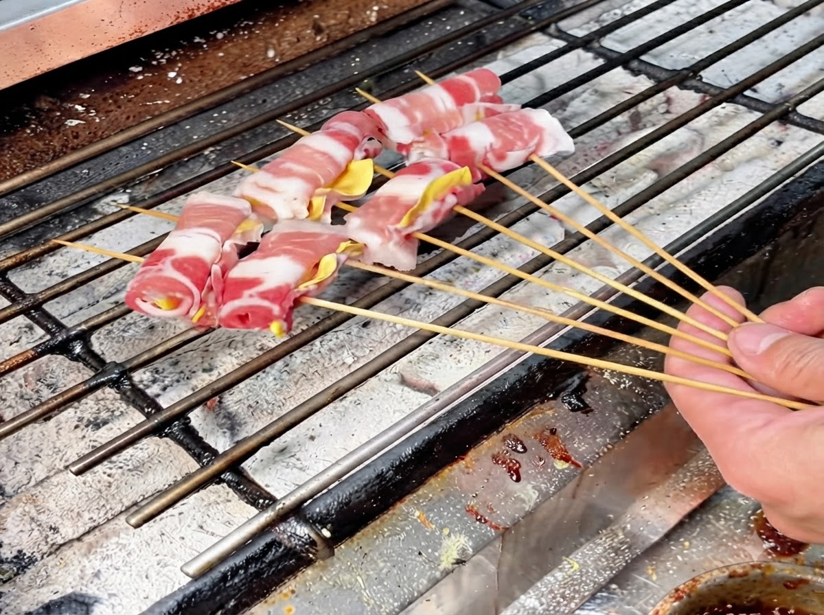 Several skewered meat rolls arranged on a hot charcoal grill grate for slow roasting.