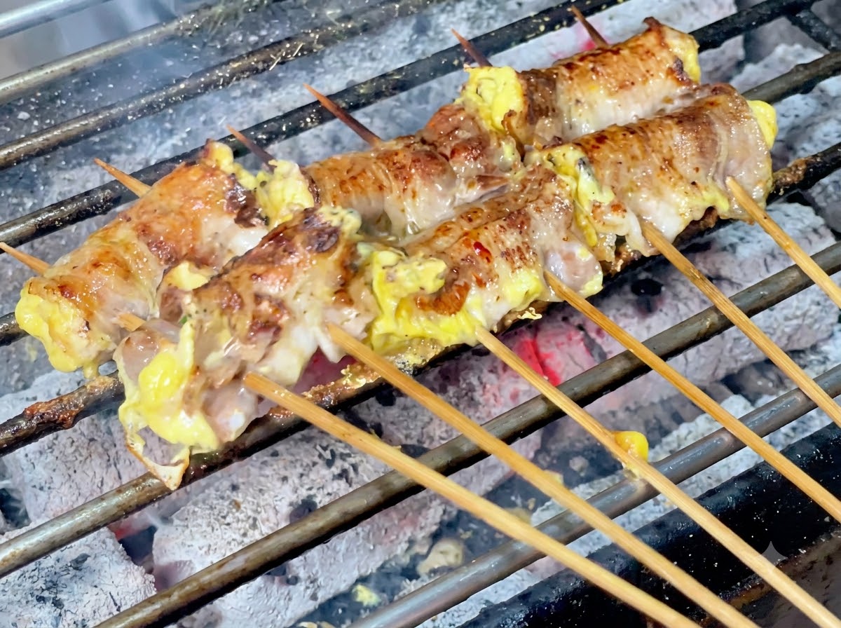 Chili powder being sprinkled over the sizzling meat rolls on the charcoal grill.