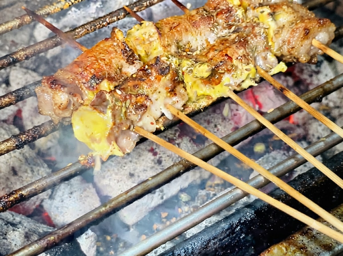 Sesame seeds being sprinkled on top of the grilled meat rolls.