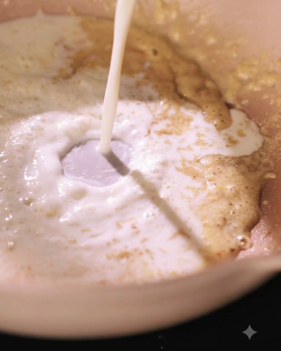 Milk being poured into a pan with a roux mixture, creating a vortex.