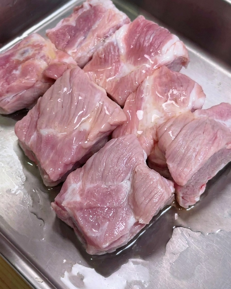 Pork ribs in a metal tray seasoned with soy sauces, oyster sauce, and pepper.