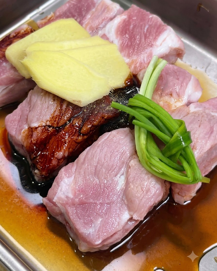 Pork ribs being marinated with ginger slices, green onions, and sauces in a tray.