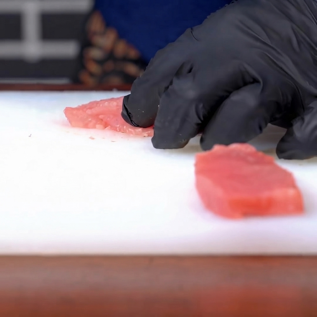 Salt and pepper being sprinkled onto a seasoned raw pork cutlet.