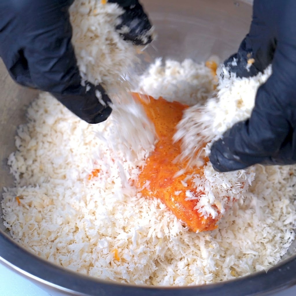 A pork cutlet being covered with a thick layer of breadcrumbs inside a large bowl.