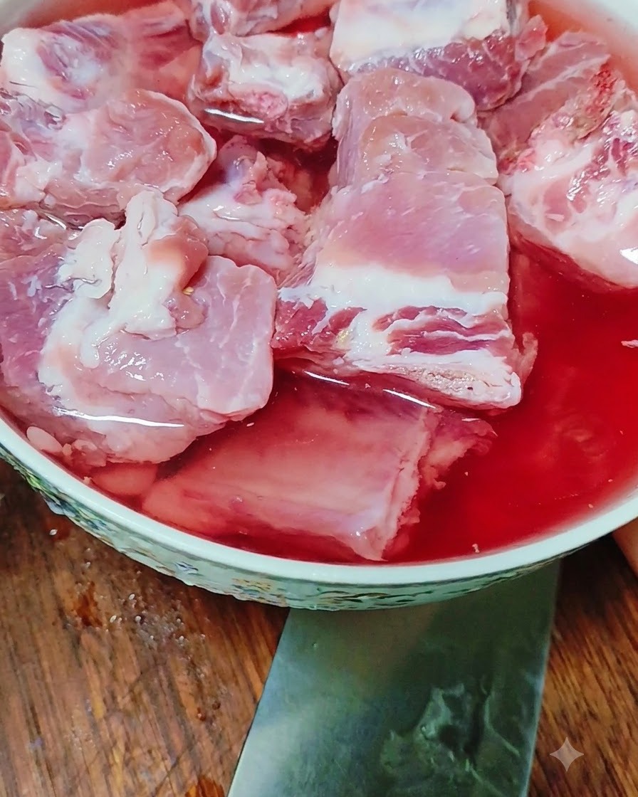 Raw pork ribs soaking in a bowl filled with red-tinted water.
