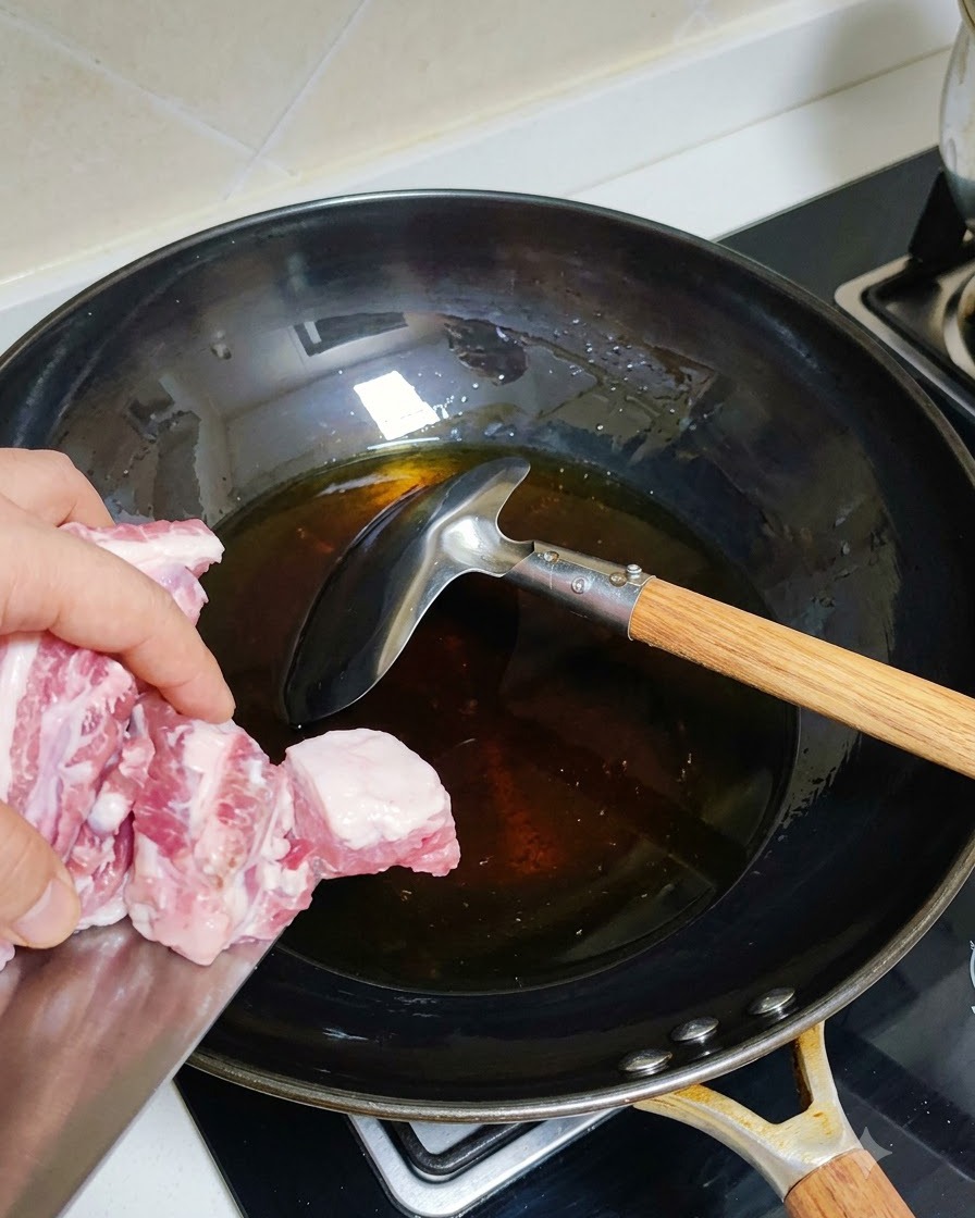 Blanched pork ribs being added to a hot wok with oil.