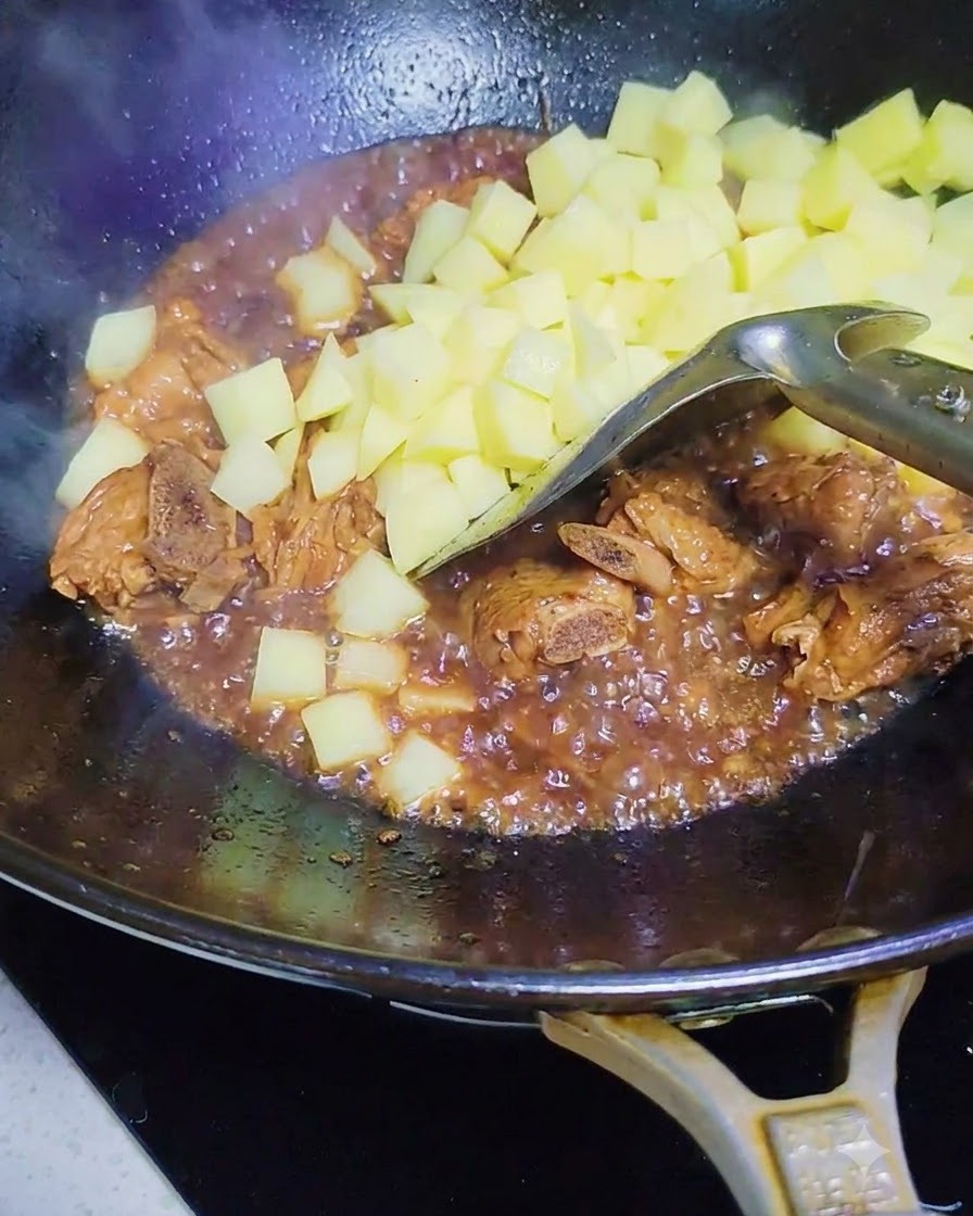 Diced raw potatoes being added into the wok with the pork ribs and sauce.