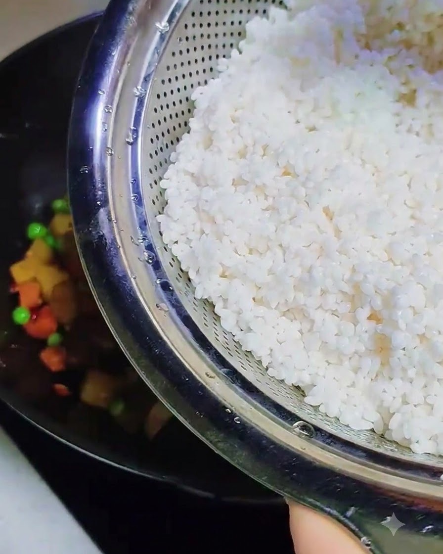 Soaked, soft sticky rice being poured from a metal colander into the wok containing the other cooked ingredients.