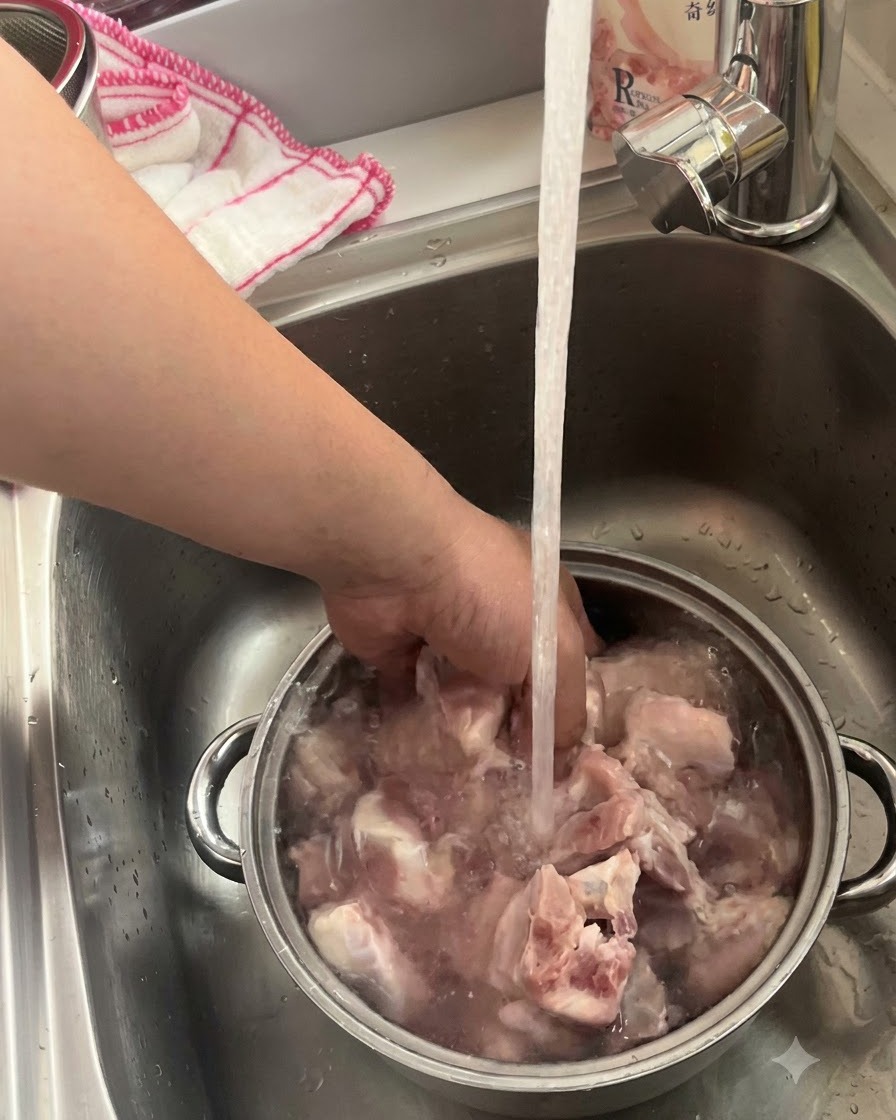 Pork ribs soaking and being washed in a metal bowl under a running kitchen faucet.