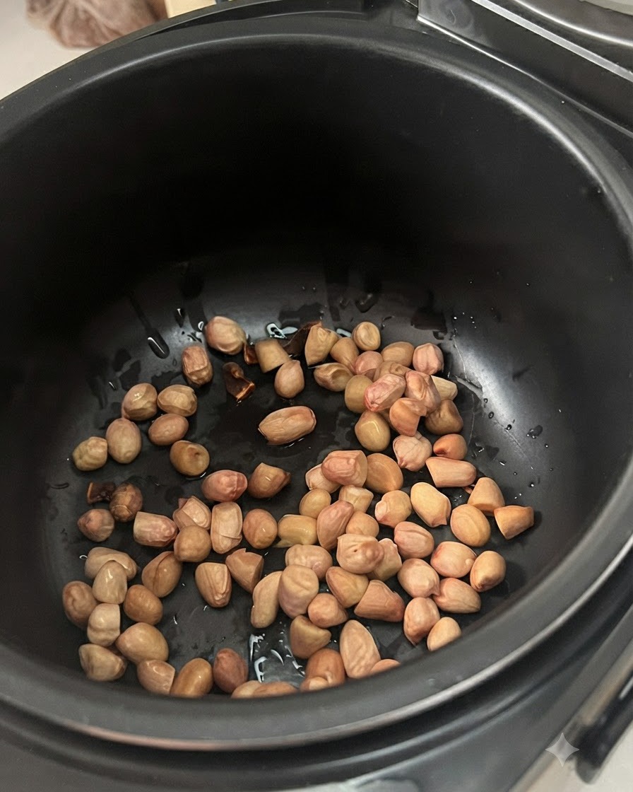 Pre-soaked peanuts scattered at the bottom of a dark electric stew pot.