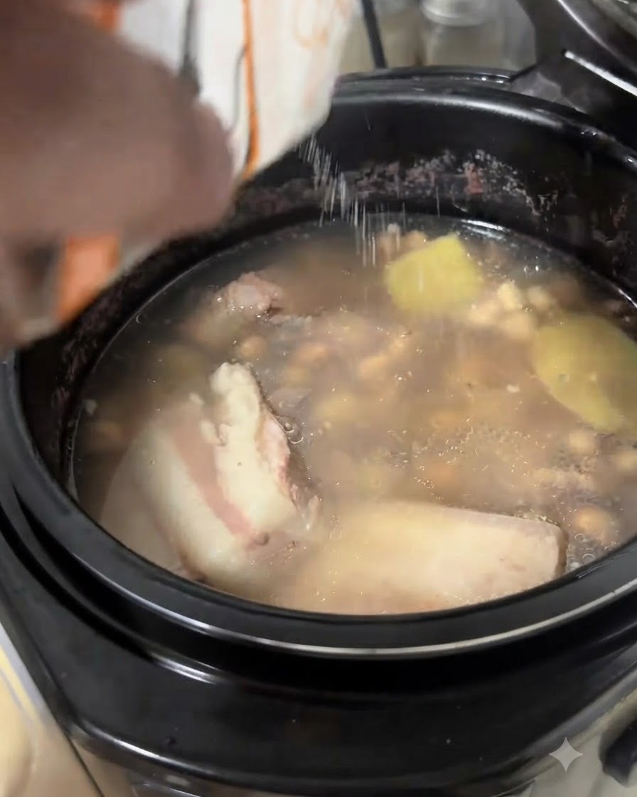 Salt being poured from a white packet into a simmering pot of pork rib and peanut soup.