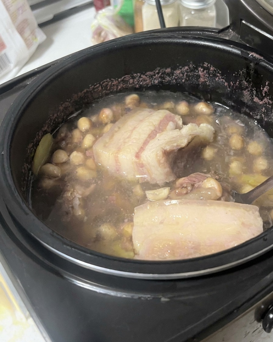 Pork belly being lifted and examined with a spoon inside the broth mixture.