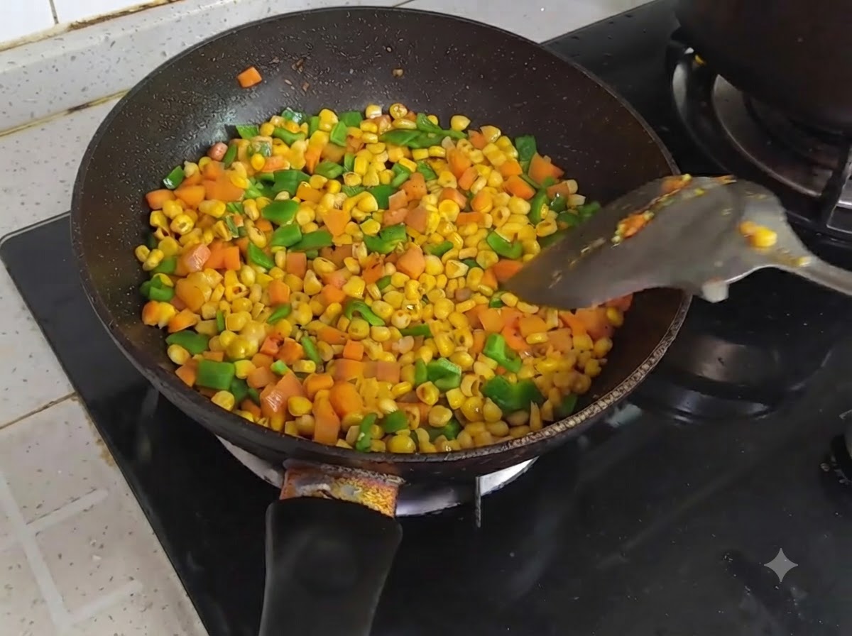 A pan filled with colorful stir-fried diced corn, carrots, and green bell peppers being tossed with a spatula.