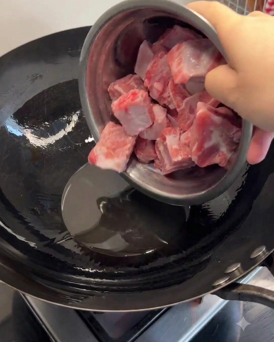 Pork ribs being added to melted lard in a heated wok and stir-fried until browned.