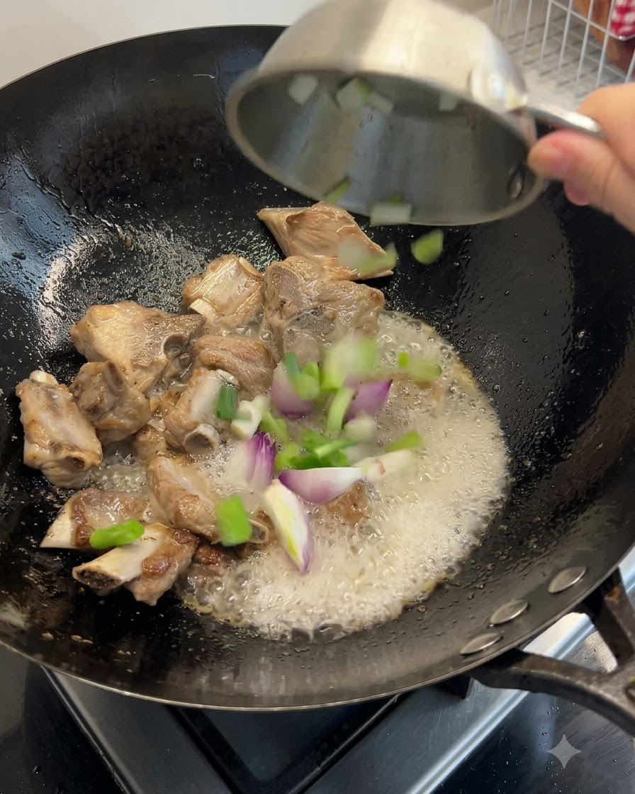 Green onions, ginger, and dried seafood ingredients being tossed into the wok with the ribs.