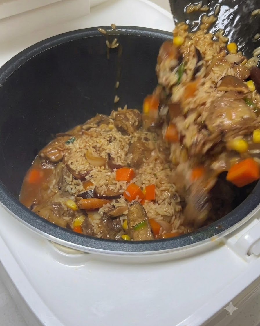 A spatula transferring seasoned rice, ribs, and vegetables into a rice cooker pot while water is being poured in.