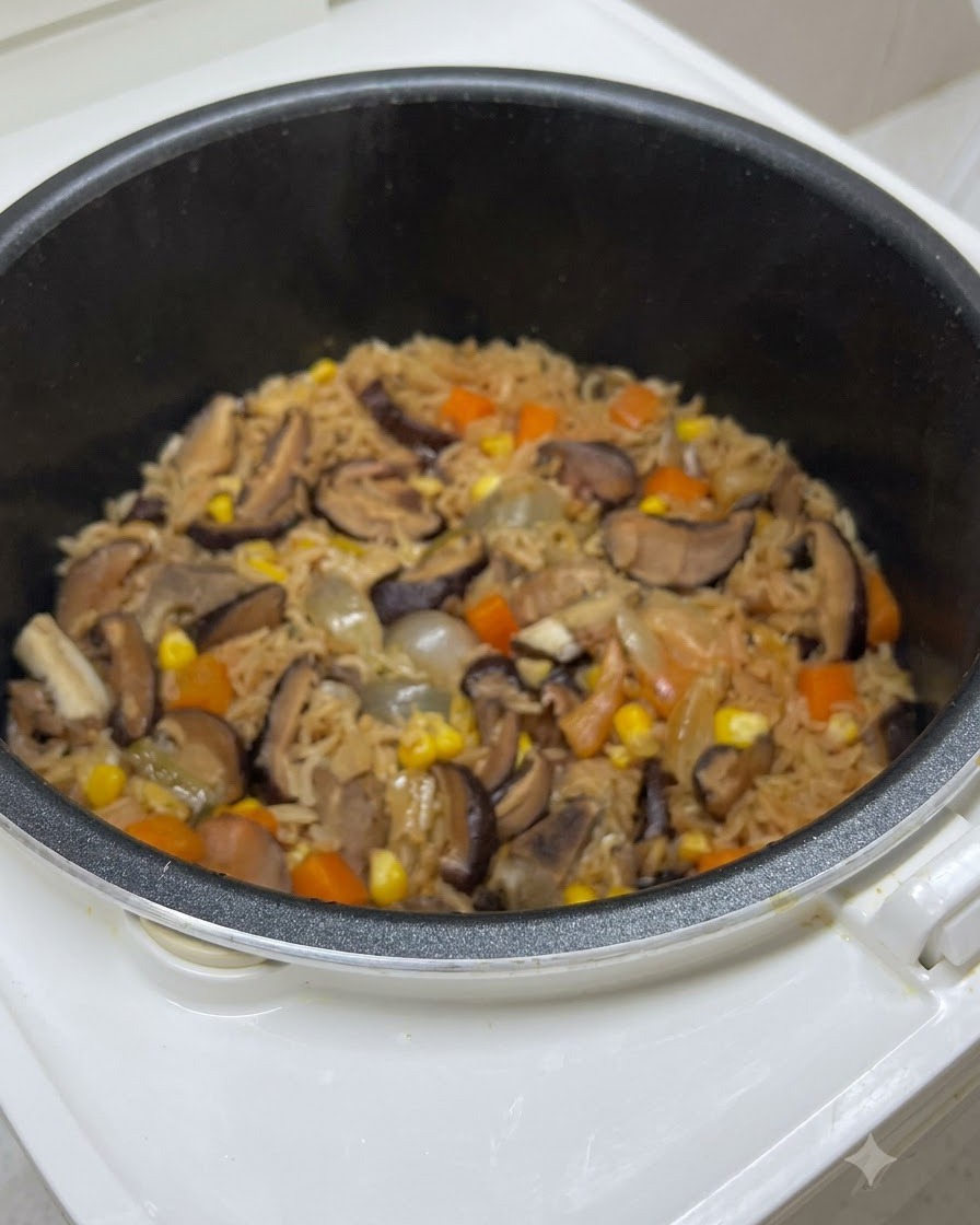 Cooked rice mixed with mushrooms, carrots, and corn inside the rice cooker pot right before final seasoning.