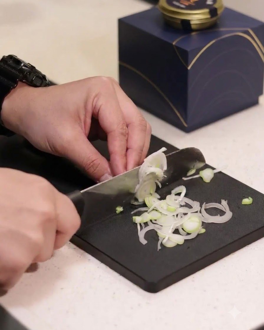 Green onions being sliced into thin rings on a black cutting board.