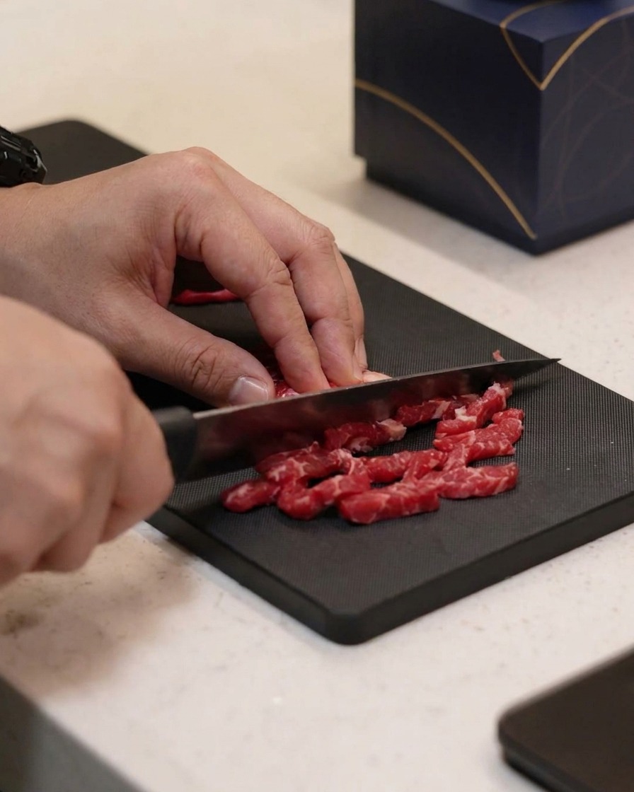 Small beef strips being seasoned with oil, salt, and pepper on a cutting board.