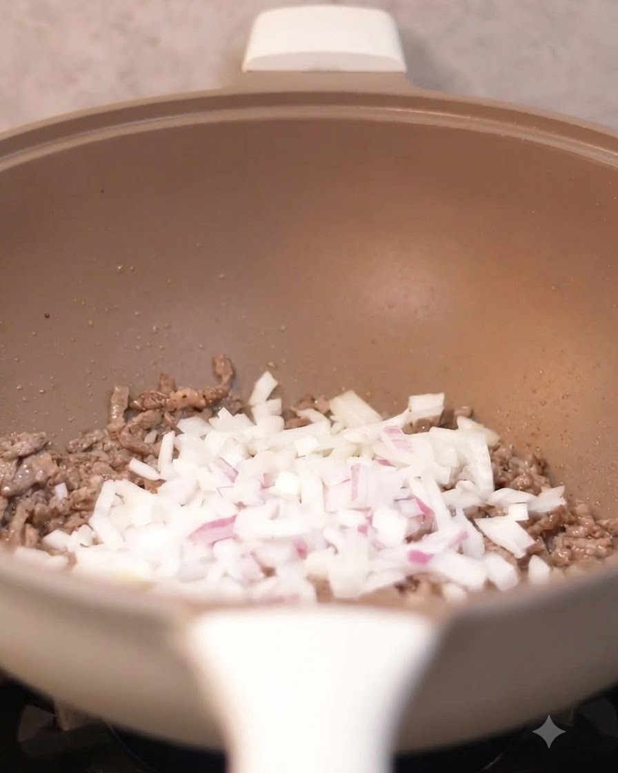 Diced onions being poured into the wok with cooked beef pieces.