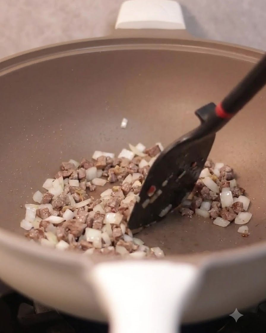 A spatula stirring scrambled eggs combined with beef and onions in a frying pan.