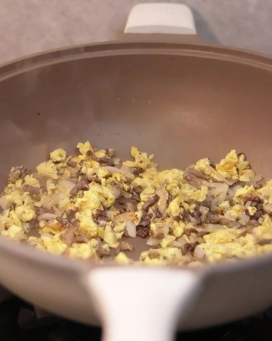 Truffle sauce being spooned into the pan containing beef, onions, and eggs.