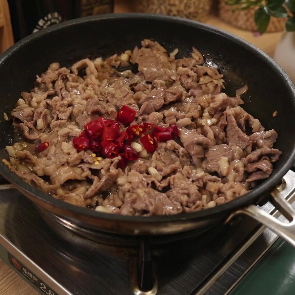 Cooked spaghetti noodles being added into a pan with beef and sliced red chili peppers.