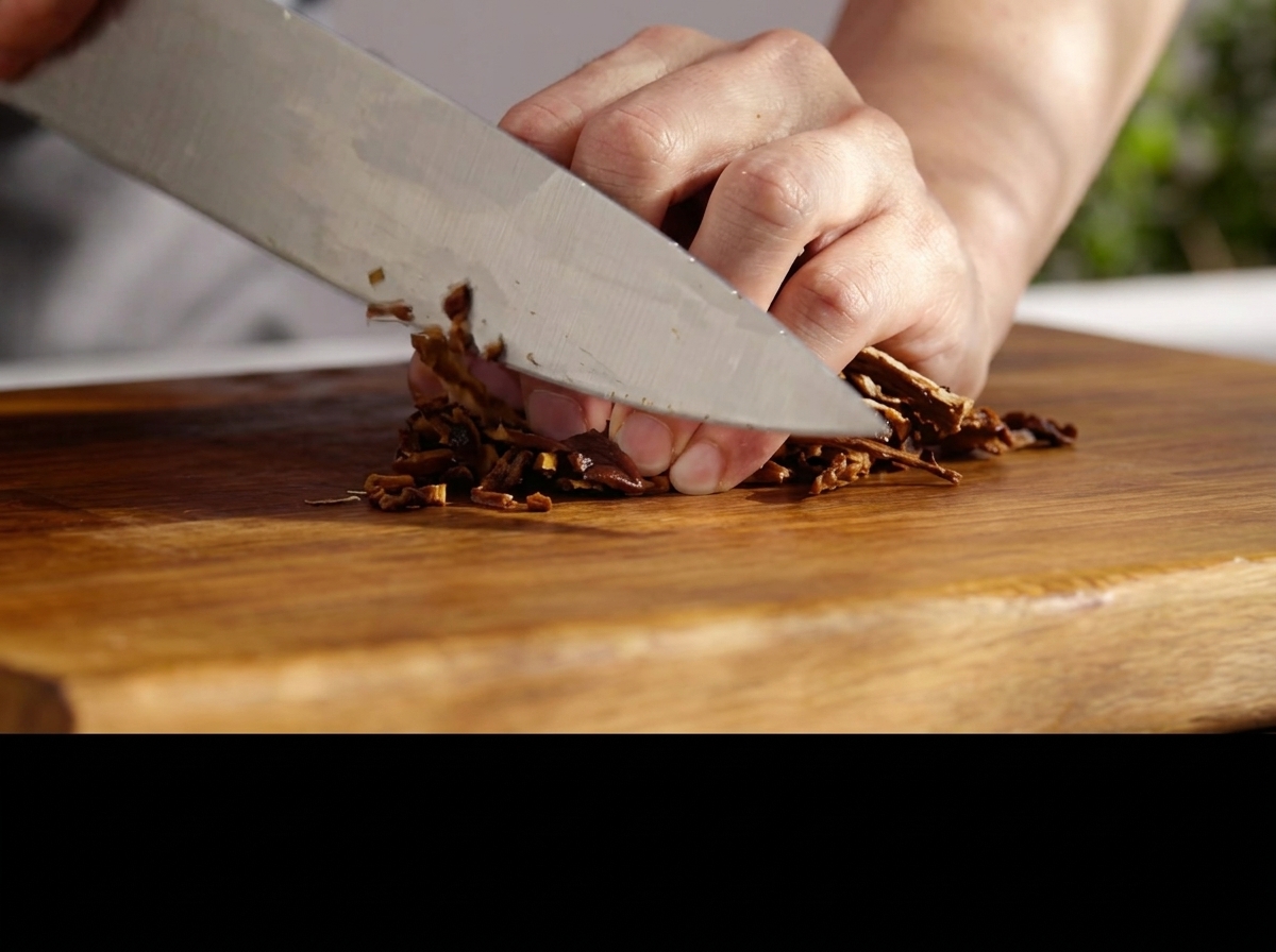 A knife chopping rehydrated mushrooms finely on a wooden board.