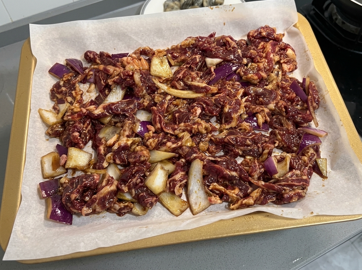Marinated beef and onion slices laid out evenly on a parchment-lined baking sheet.