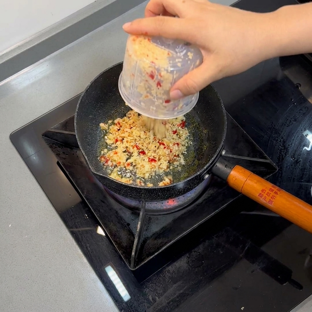 Minced garlic and red chilies frying in hot oil inside a small pan.
