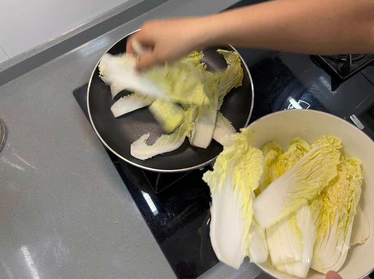 Chinese cabbage leaves being placed to form a bottom layer inside a frying pan.