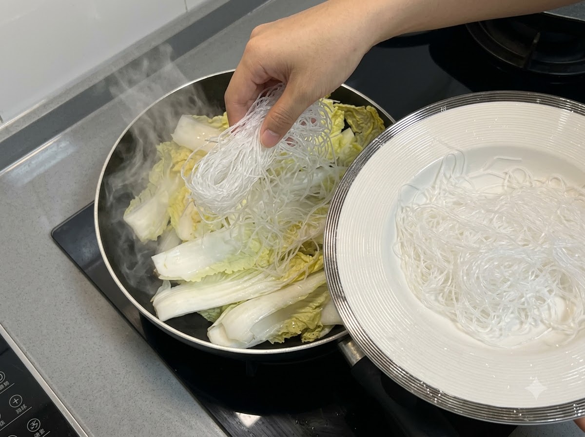 Vermicelli noodles being placed on top of the Chinese cabbage inside the pan.