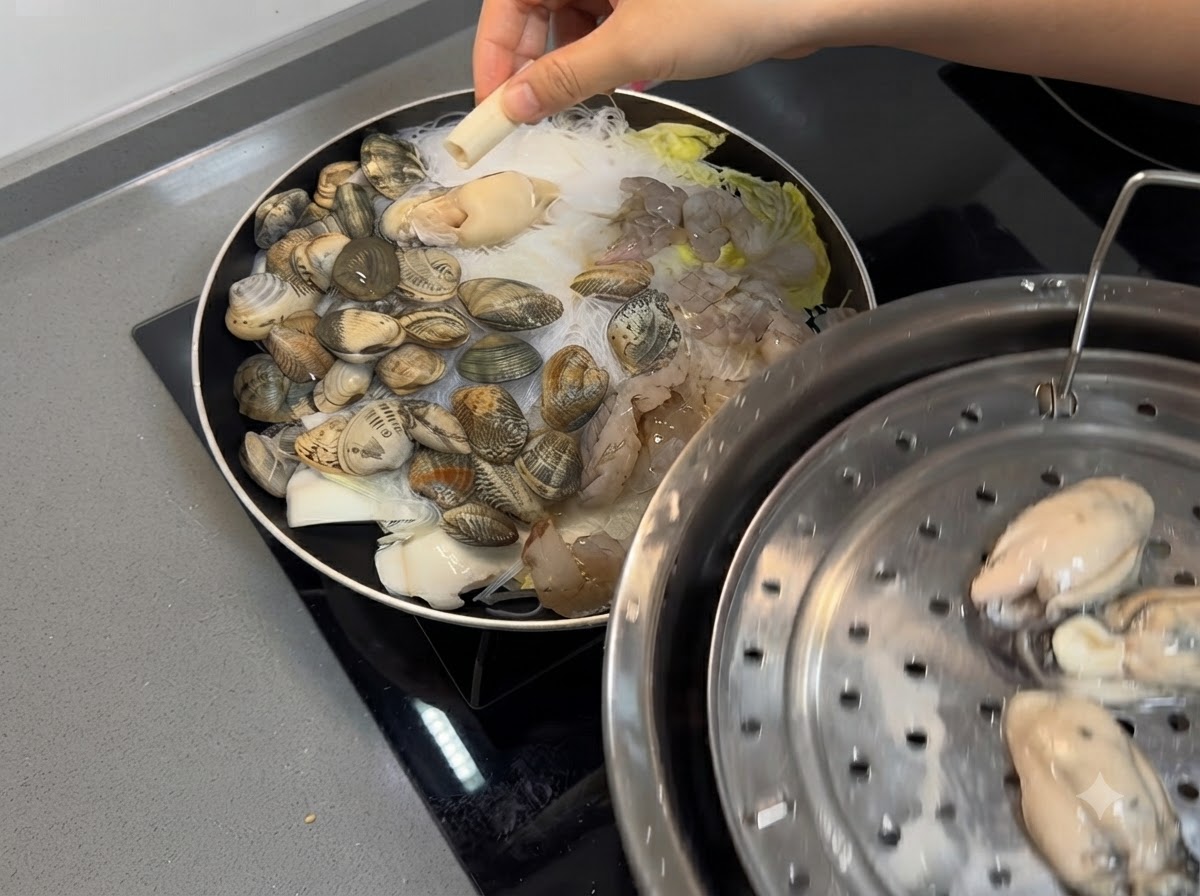 Shrimp and fresh oysters being placed onto the seafood and noodle mixture in the pan.