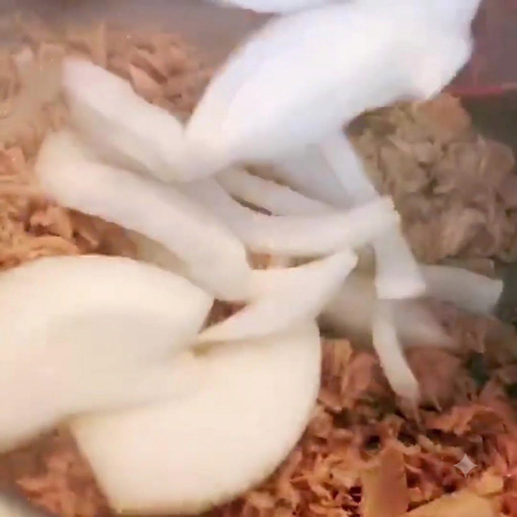 Sliced onions being added into the pot containing tuna and stirred.