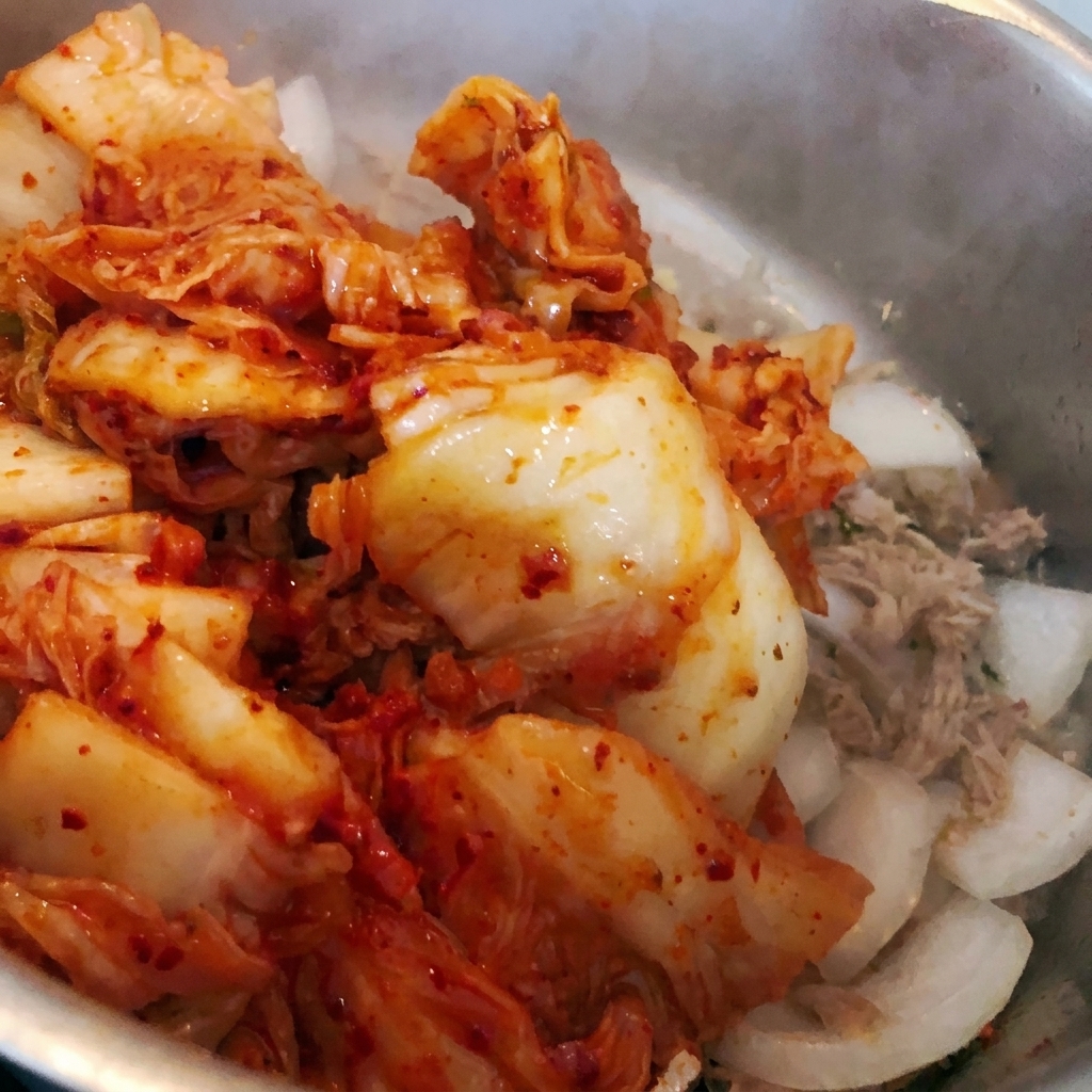 Chopped kimchi being tossed into the pot with the existing ingredients.